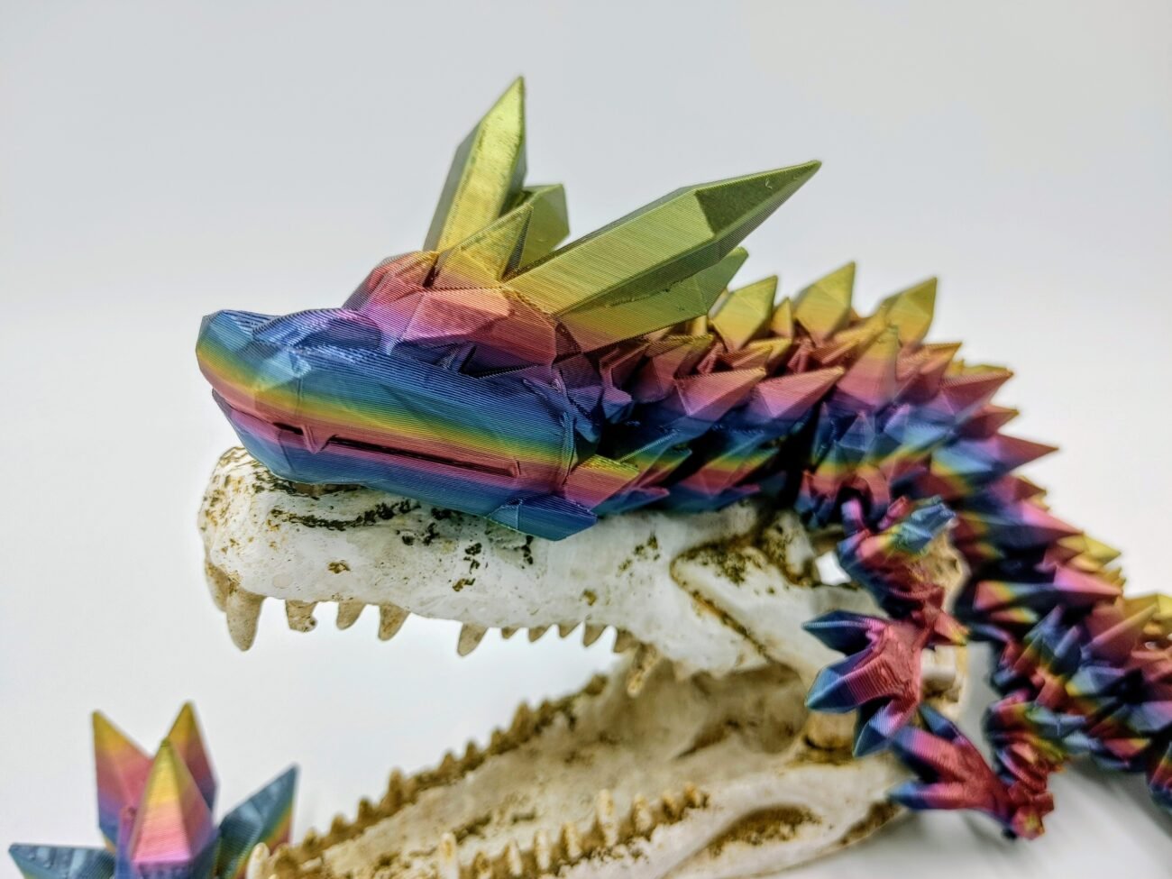 Articulated Crystal Dragon 3D Printed in Blue Mountains Rainbow Articulated Crystal Dragon Sensory Toy in Silk Blue Mountains Rainbow Sitting on a Fake Skull Closeup with a White Background