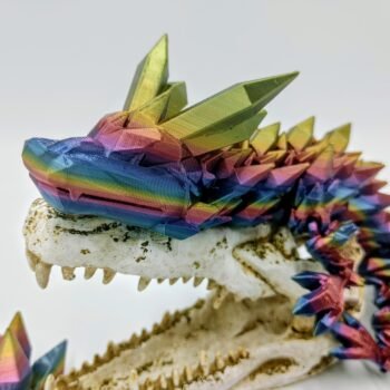 Articulated Crystal Dragon 3D Printed in Blue Mountains Rainbow Articulated Crystal Dragon Sensory Toy in Silk Blue Mountains Rainbow Sitting on a Fake Skull Closeup with a White Background