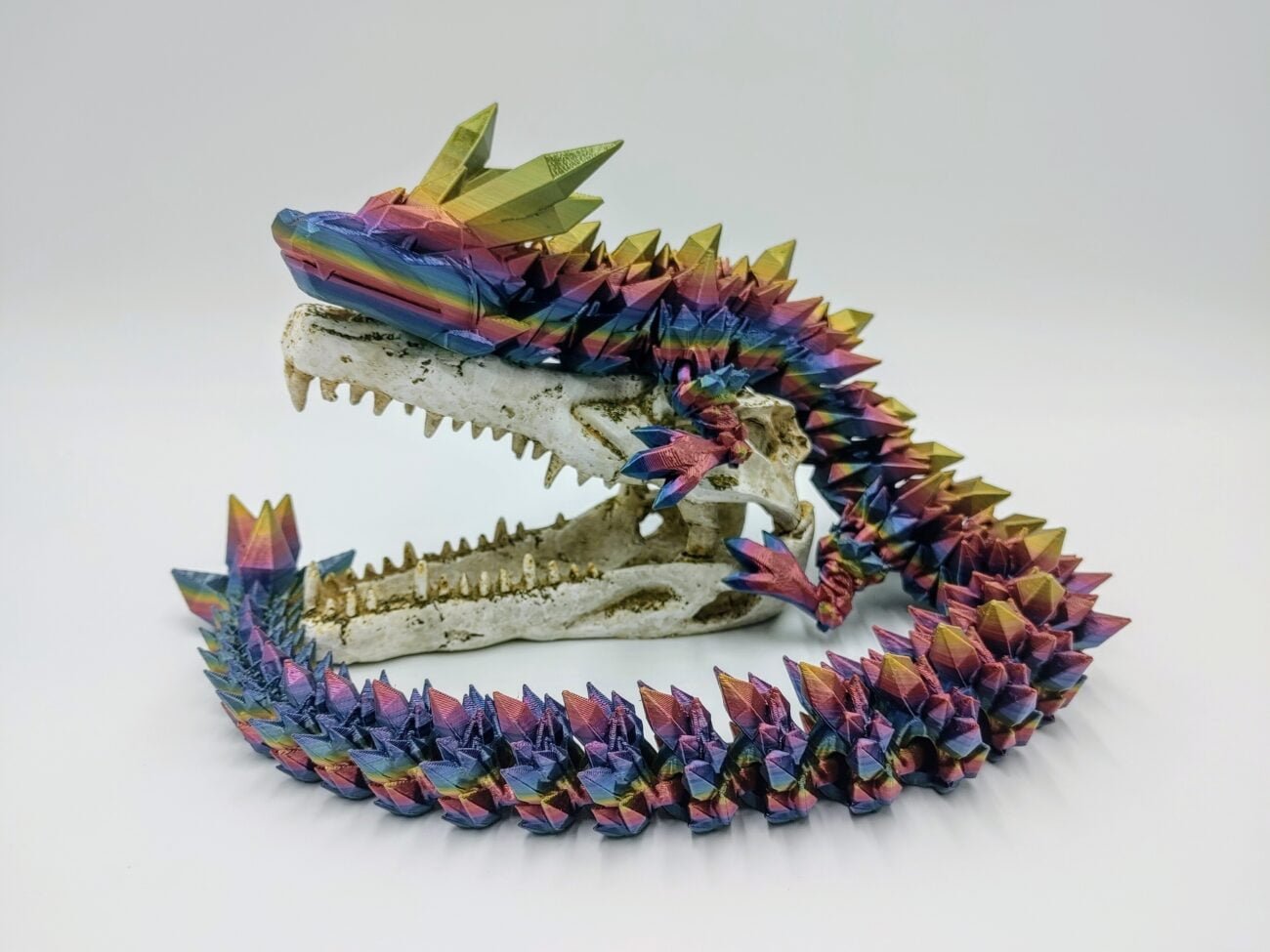 Articulated Crystal Dragon 3D Printed in Blue Mountains Rainbow Articulated Crystal Dragon Sensory Toy in Silk Blue Mountains Rainbow Sitting on a Fake Skull Closeup with a White Background
