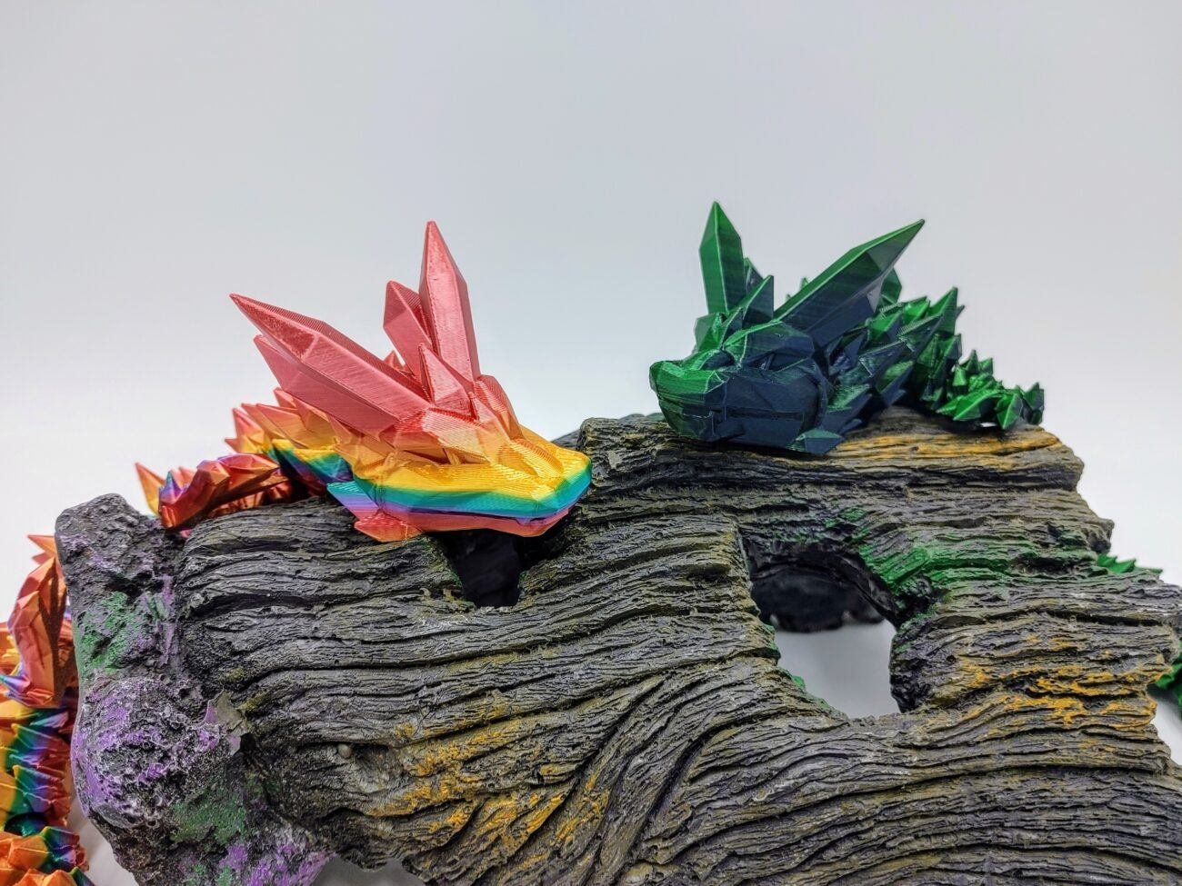 Articulated Crystal Dragon 3D Printed in Coober Pedy Rainbow and Green to Blue Articulated Crystal Dragon Sensory Toys in Silk Coober Pedy Rainbow and Green to Blue Sitting on a Log Closeup with a White Background