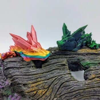 Articulated Crystal Dragon 3D Printed in Coober Pedy Rainbow and Green to Blue Articulated Crystal Dragon Sensory Toys in Silk Coober Pedy Rainbow and Green to Blue Sitting on a Log Closeup with a White Background