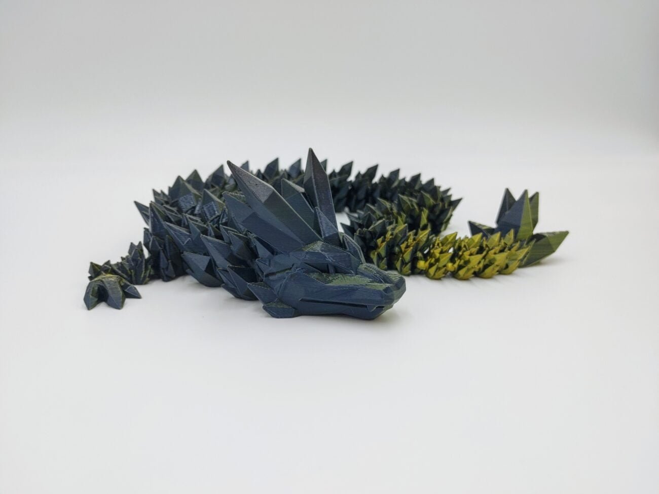 Articulated Crystal Dragon 3D Printed in Dual Silk Black to Gold Articulated Crystal Dragon Sensory Toy Designed by Cinderwing3d in Dual Silk Black to Gold with a White Background