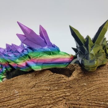 Articulated Crystal Dragon 3D Printed in Great Barrier Reef Rainbow and Black to Gold Articulated Crystal Dragon Sensory Toys in Silk Great Barrier Reef Rainbow and Black to Gold Sitting on a Log Closeup with a White Background