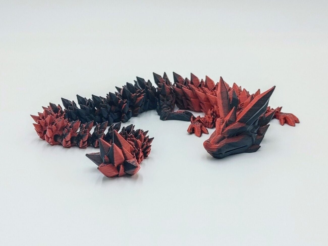 Articulated Crystal Dragon 3D Printed in Matte Black to Red Articulated Crystal Dragon Sensory Toy Designed by Cinderwing3d in Matte Black to Red with a White Background