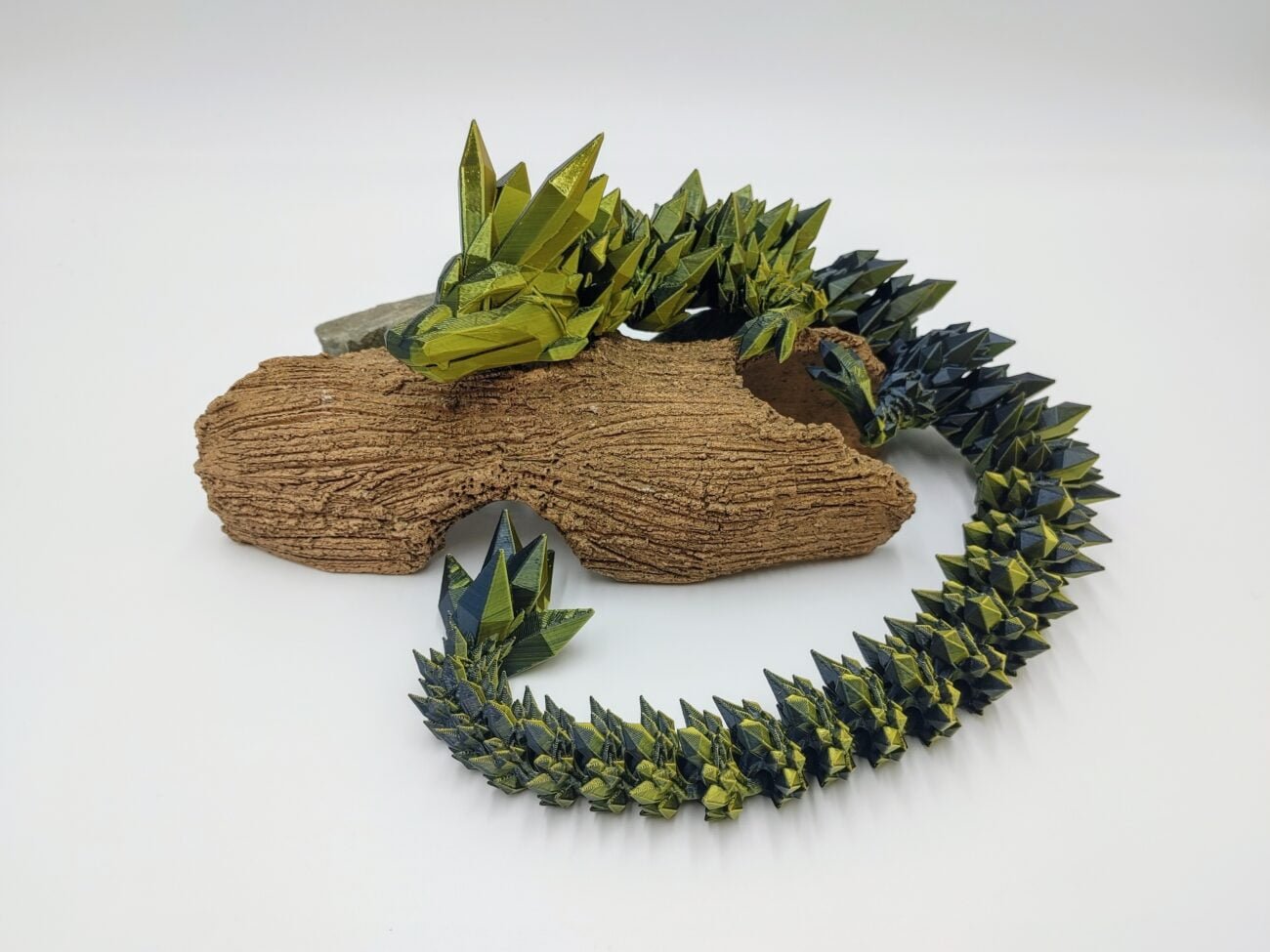 Articulated Crystal Dragon 3D Printed in Silk Black to Gold Articulated Crystal Dragon Sensory Toy in Silk Black to Gold Lying on a Log with a White Background