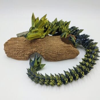 Articulated Crystal Dragon 3D Printed in Silk Black to Gold Articulated Crystal Dragon Sensory Toy in Silk Black to Gold Lying on a Log with a White Background
