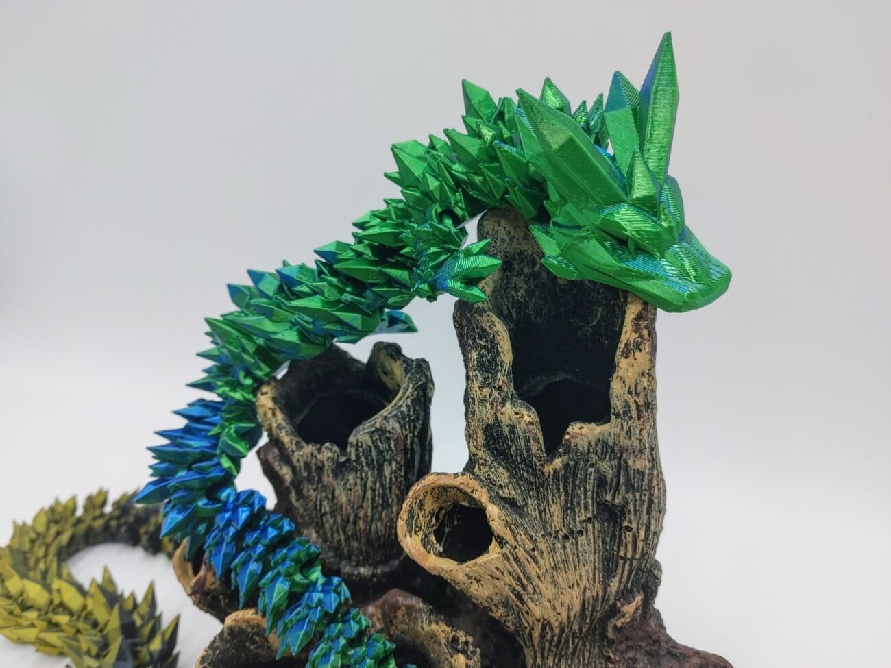 Articulated Crystal Dragon 3D Printed in Silk Blue to Green Articulated Crystal Dragon Sensory Toy in Silk Blue to Green Sitting on Coral with a White Background