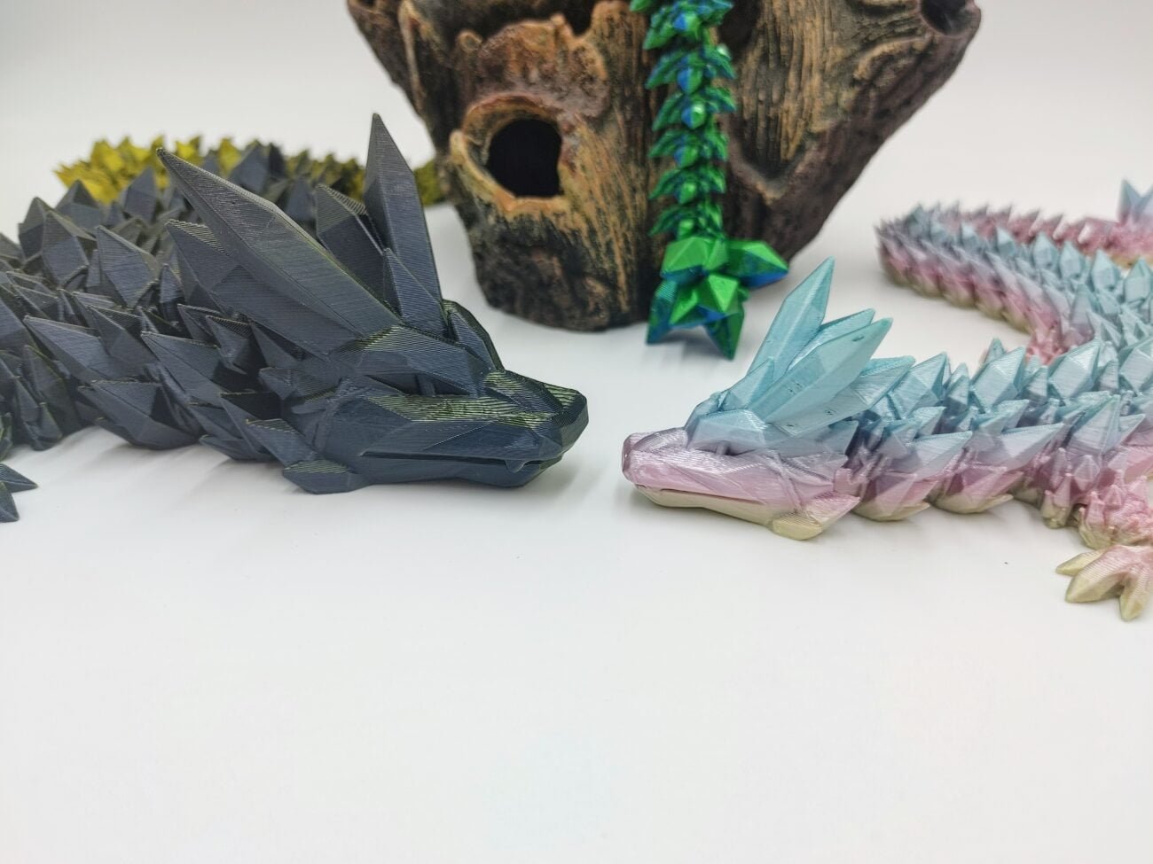 Articulated Crystal Dragons 3D Printed in Uluru Rainbow and Black to Gold Articulated Crystal Dragon Sensory Toys in Silk Uluru Rainbow and Black to Gold with a White Background Looking at Each Other