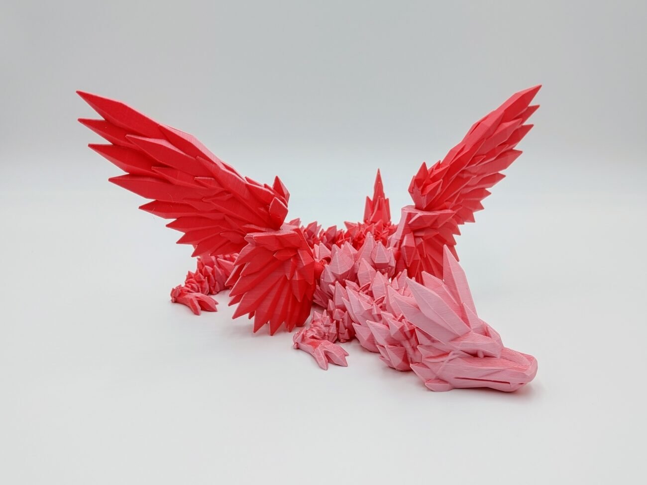 Articulated Crystalwing Dragon 3D Printed Designed by Cinderwing3d in Matte Pink to Red Articulated Crystalwing Dragon Sensory Toy Designed by Cinderwing3d in Matte Pink to Red with a White Background