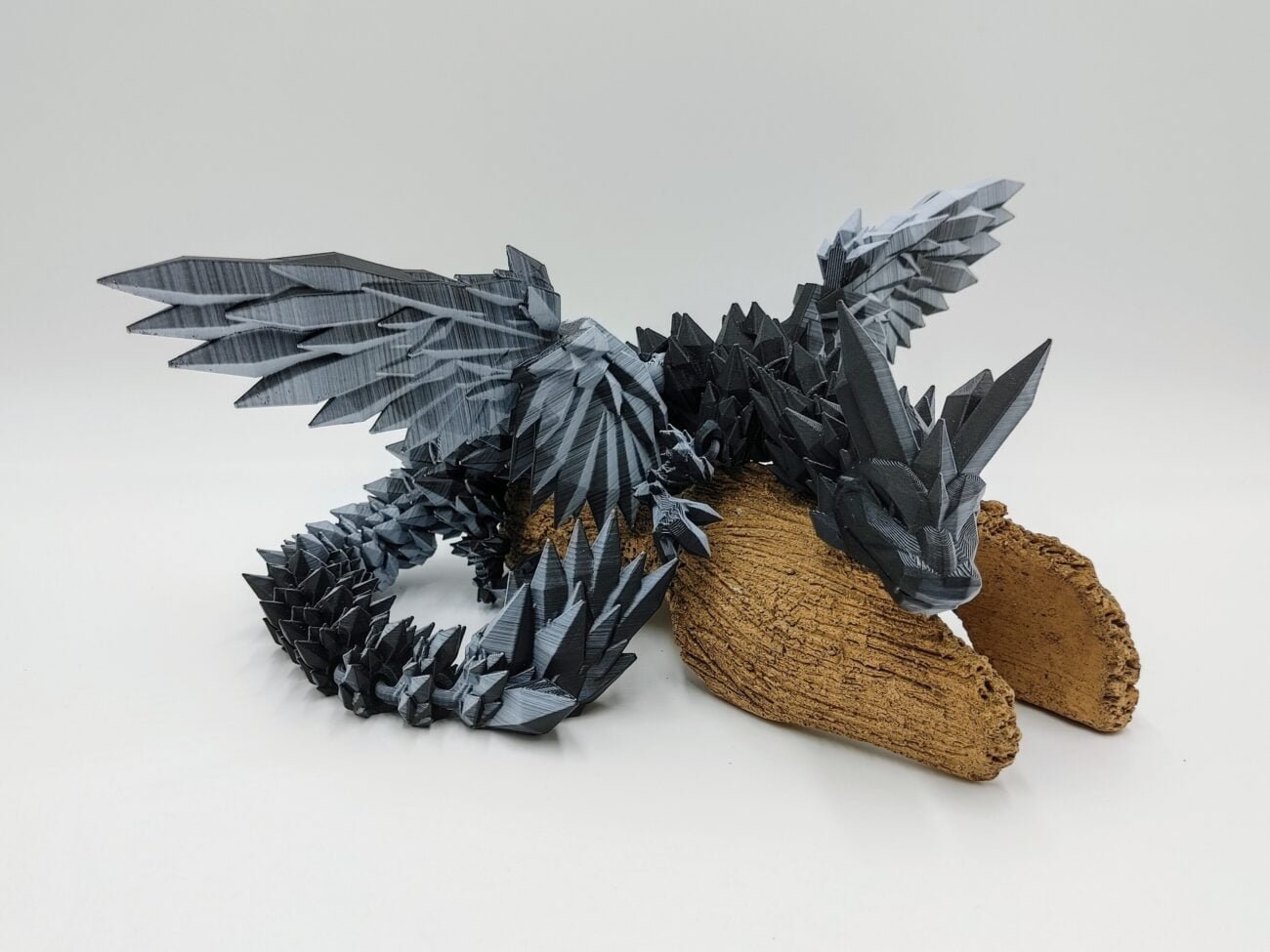 Articulated Crystalwing Dragon 3D Printed in Matte Black to White Articulated Crystalwing Dragon Sensory Toys in Matte Black to White Sitting on a Log with a White Background