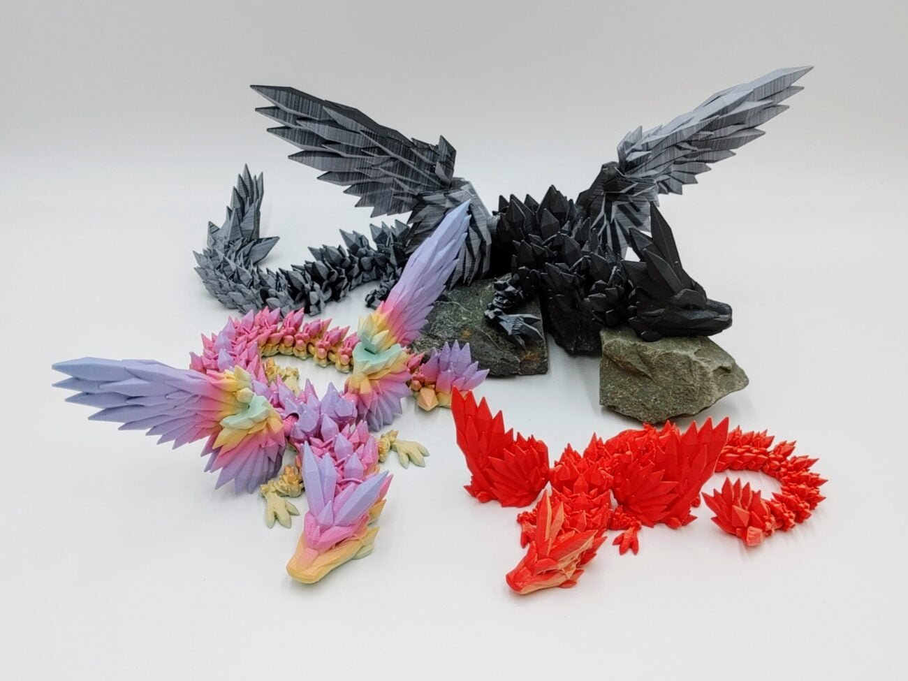 Articulated Crystalwing Dragon 3D Printed in Matte Dual Tone Hues and Rainbows Articulated Crystalwing Dragon Sensory Toys in Matte Dual Tone Hues and Rainbows Sitting on Rocks with a White Background