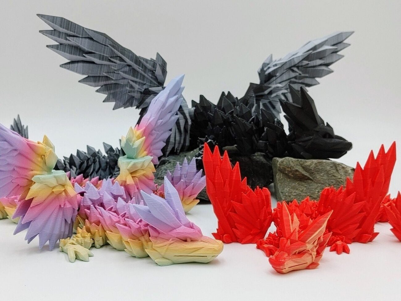 Articulated Crystalwing Dragon 3D Printed in Matte Dual Tone Hues and Rainbows Articulated Crystalwing Dragon Sensory Toys in Matte Dual Tone Hues and Rainbows Sitting on Rocks with a White Background Closeup