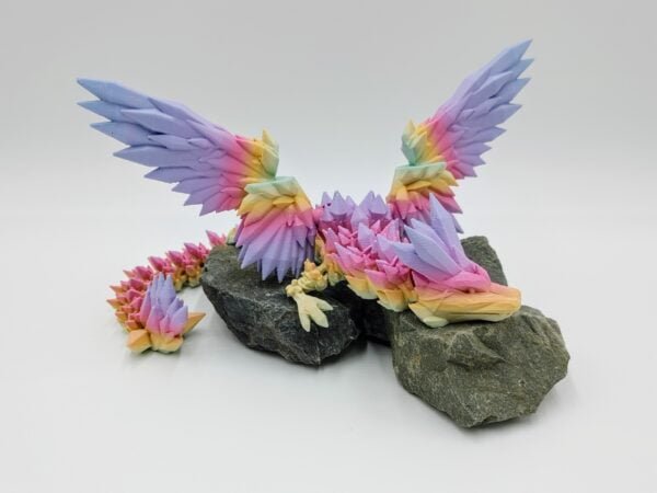 Articulated Crystalwing Dragon 3D Printed in Matte Pastal Rainbow Articulated Crystalwing Dragon Sensory Toys in Matte Pastal Rainbow Sitting on Rocks On a White Background