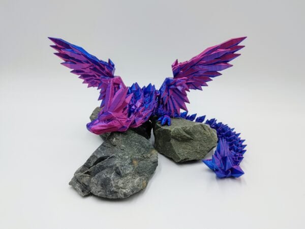 Articulated Crystalwing Dragon 3D Printed in Silk Blue to Purple Articulated Crystalwing Dragon Sensory Toys in Silk Blue to Purple Sitting on Rocks with a White Background