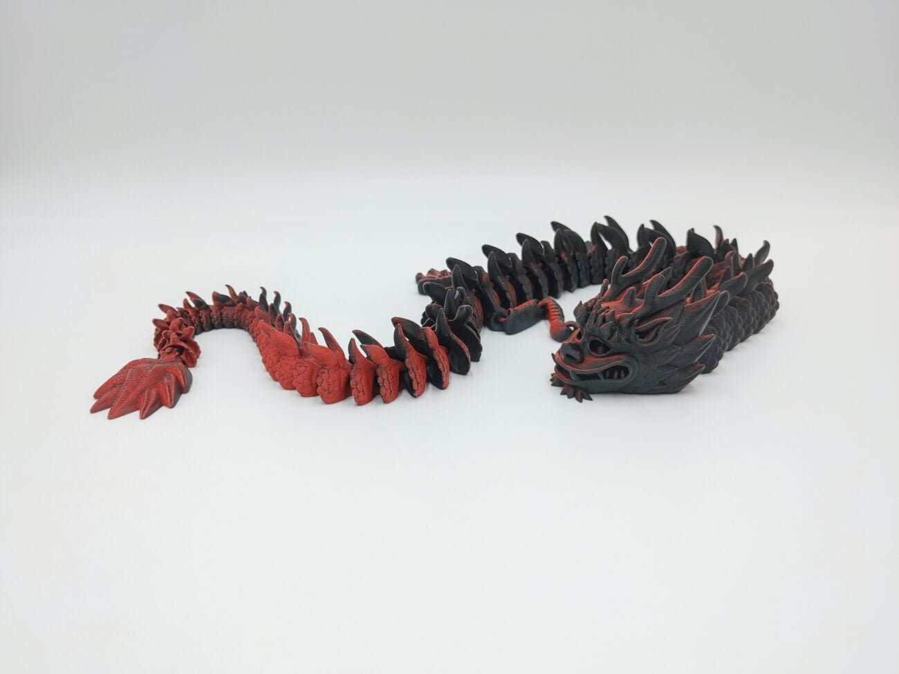 Articulated Imperial Dragon 3D Printed in Matte Red to Black Articulated Imperial Dragon Sensory Toys Designed by Flexy Factory in Matte Red to Black with a White Background