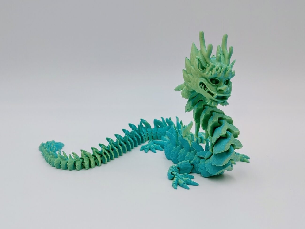 Articulated Imperial Dragon 3D Printed in Matte Teal to Yellow Articulated Imperial Dragon Sensory Toys in Matte Teal to Yellow with a White Background