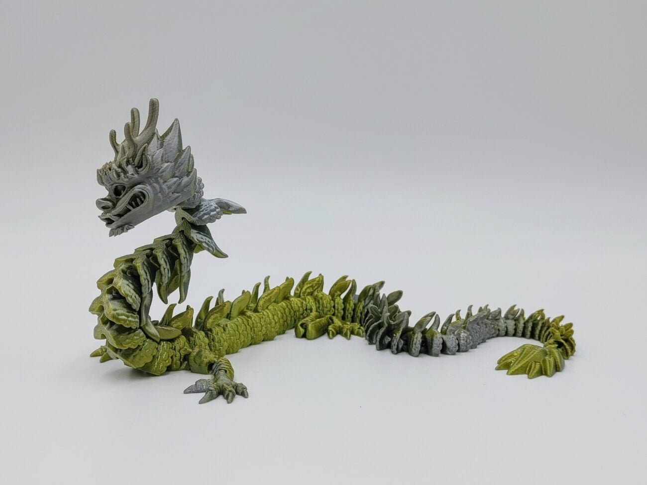 Articulated Imperial Dragon 3D Printed in Silk Silver to Bronze Articulated Imperial Dragon Sensory Toys Designed by Flexy Factory in Silk Silver to Bronze with a White Background